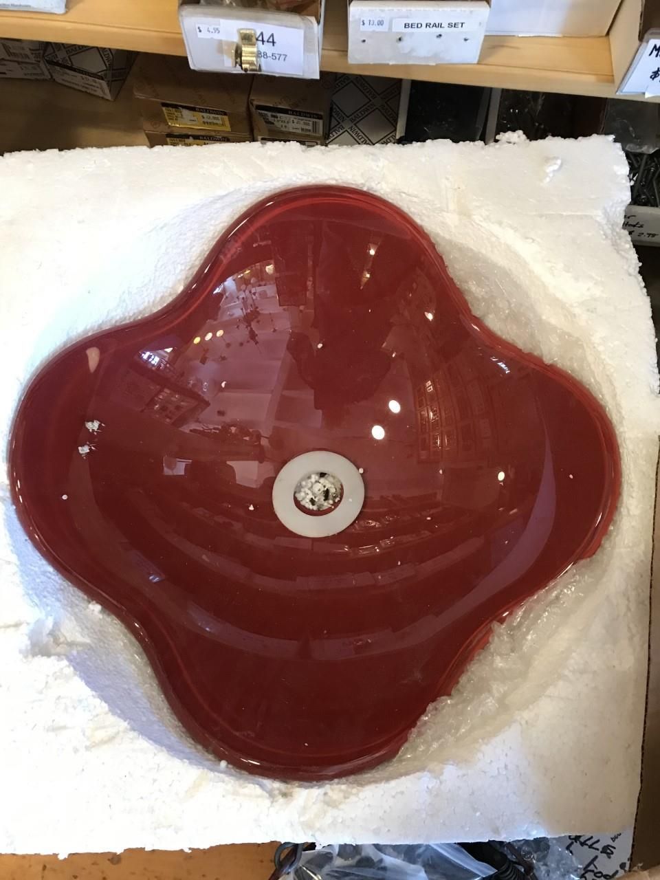 Red glass bathroom sink, flower-shaped with white drain, in protective packaging.