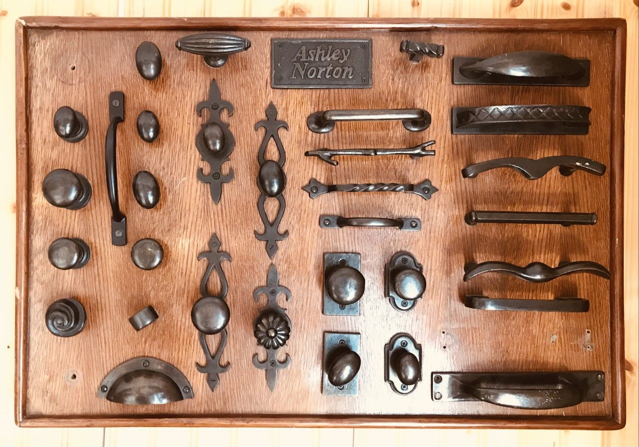 Wooden display board with various black metal door handles, knobs, and pulls.