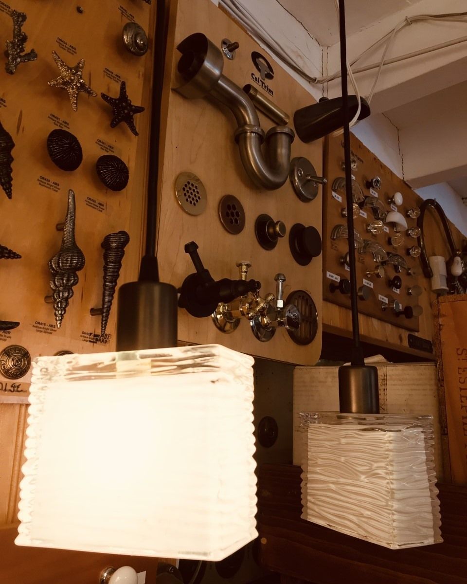Two pendant lights with textured white shades hang in a hardware store