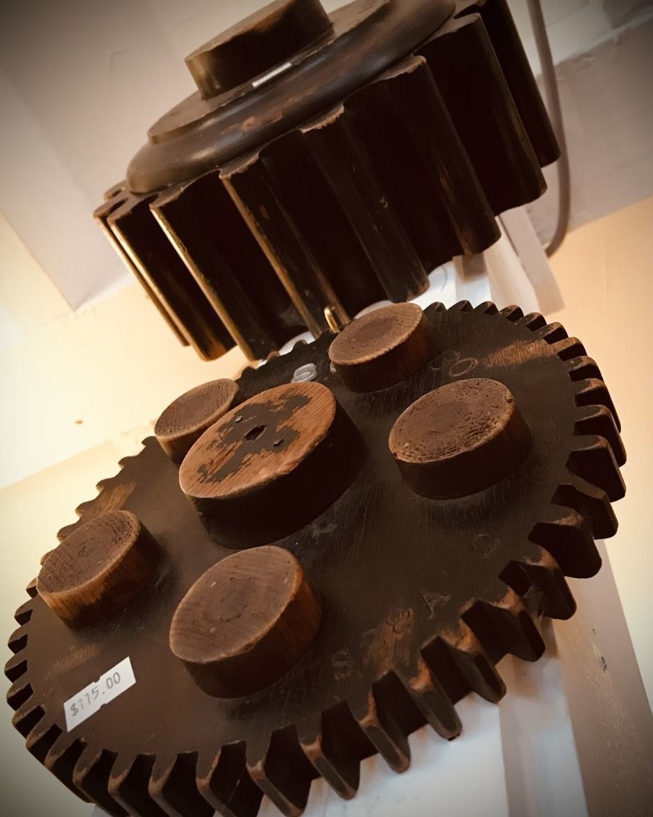 Two dark metal gears meshed together. One larger gear has cylindrical brown components attached.