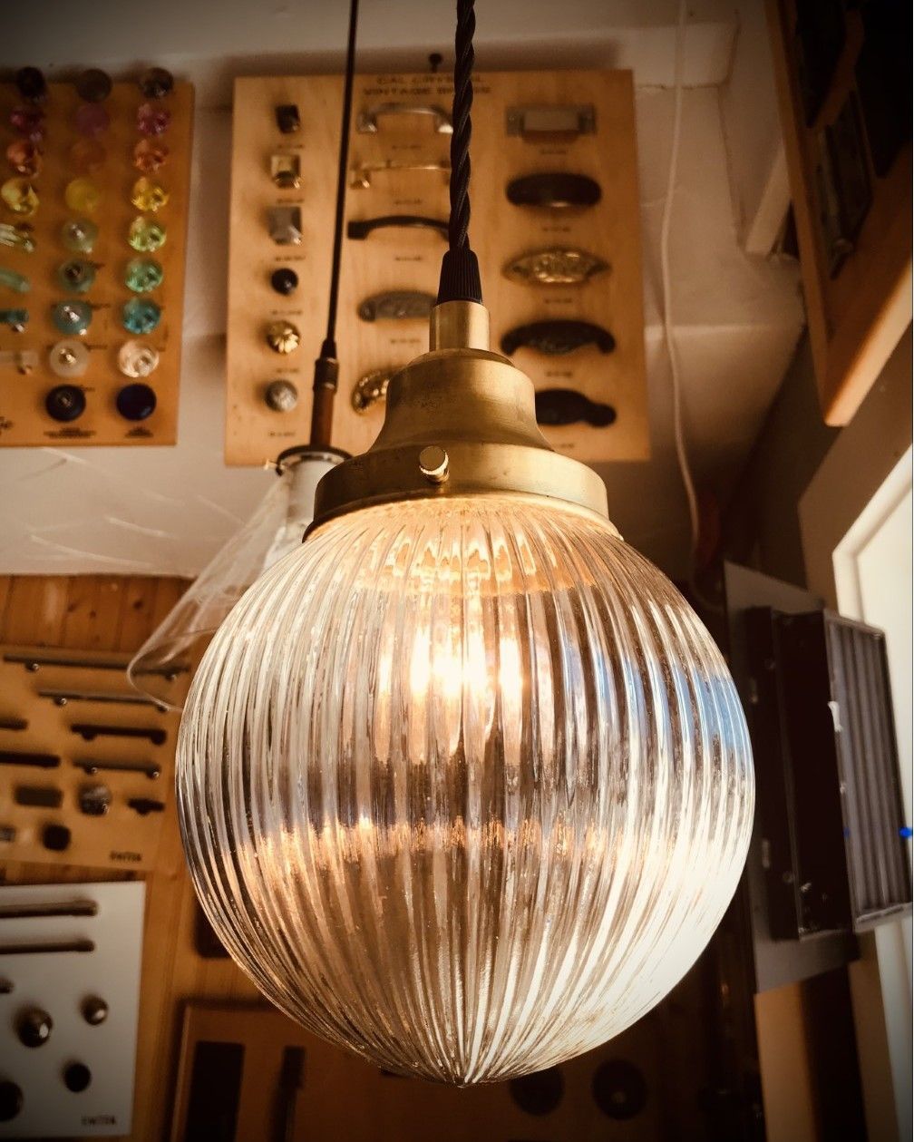 Clear, ribbed glass pendant light with brass fixtures, hanging in a workshop.