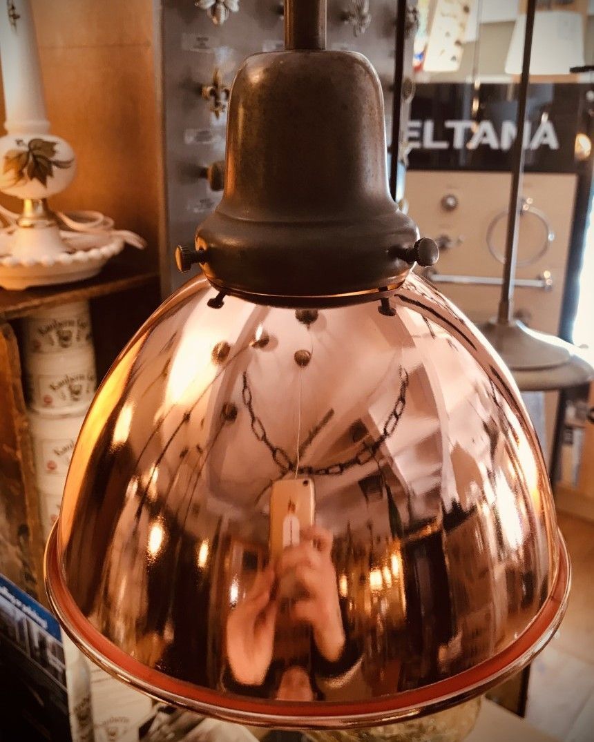 Copper-colored pendant lamp with reflective surface, in a shop setting.