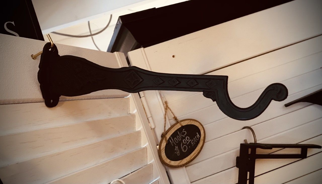 Black decorative bracket mounted on white slatted wall, holding an oval sign.