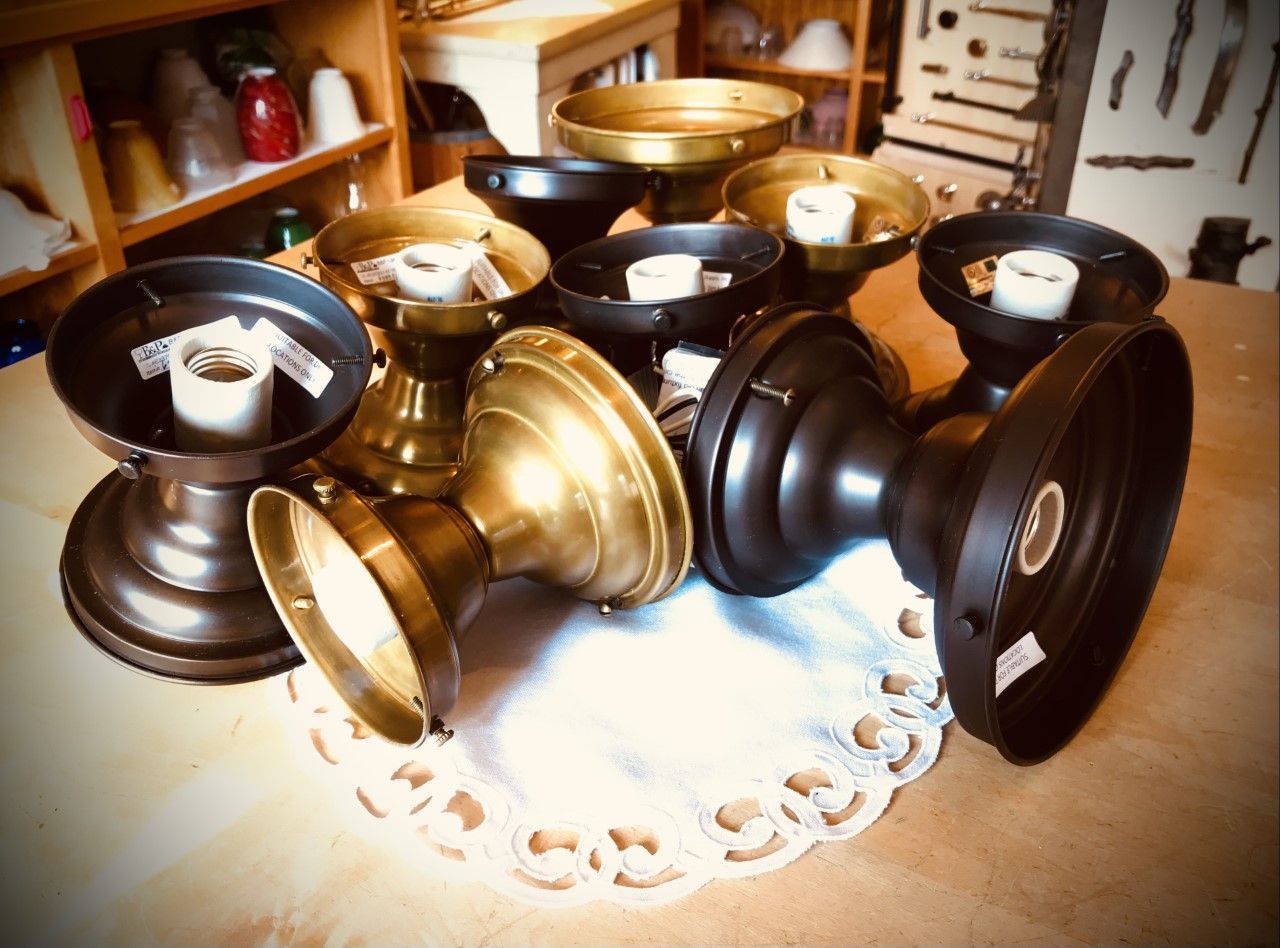 Overhead light fixtures in various colors (bronze, brass, black) arranged on a doily.