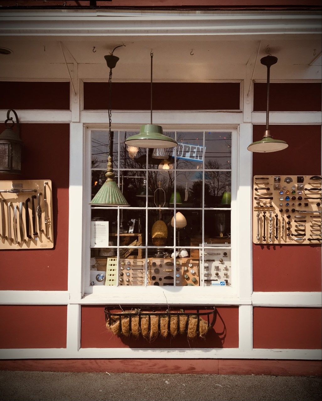 Red storefront with a window displaying various items, including lamps and tools, with an open sign.