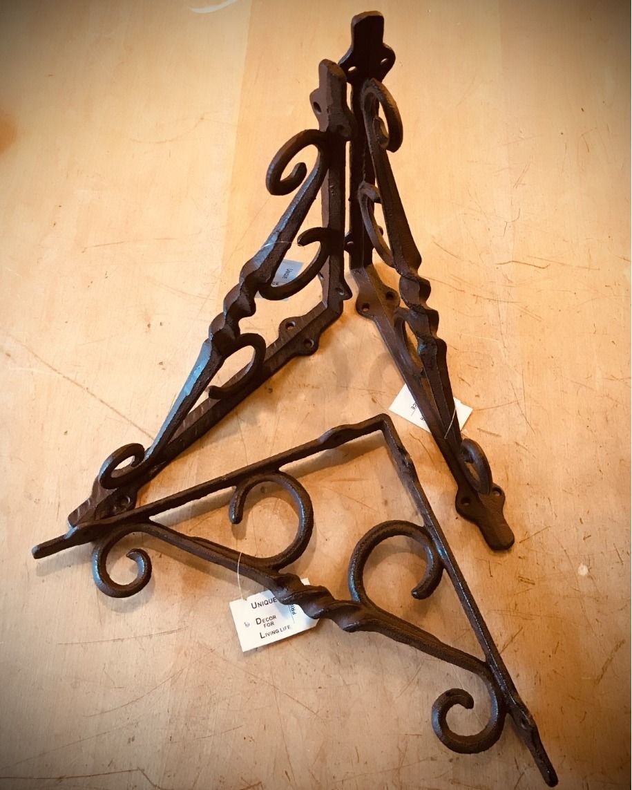 Two ornate, dark metal plant hangers sit on a light-colored surface.