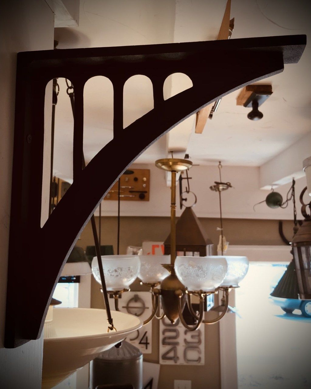 Dark wood bracket with curved design, attached to a wall, supporting an overhanging light fixture.