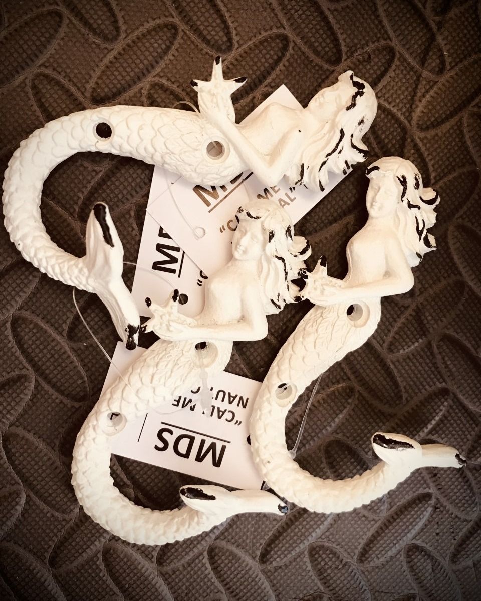 White mermaid ornaments, coiled snake-like, with tags against a textured brown surface.