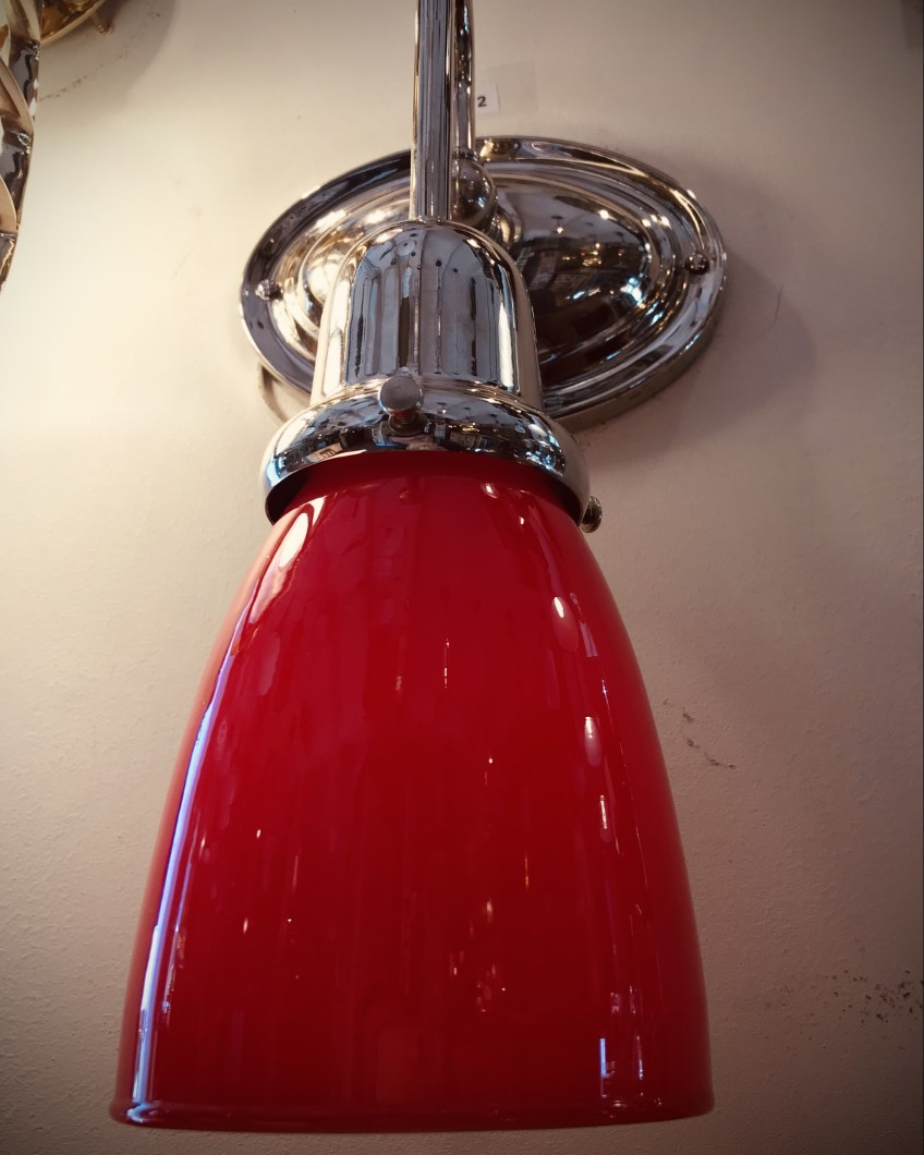 Red glass cone-shaped wall light with chrome fixture on a white wall.