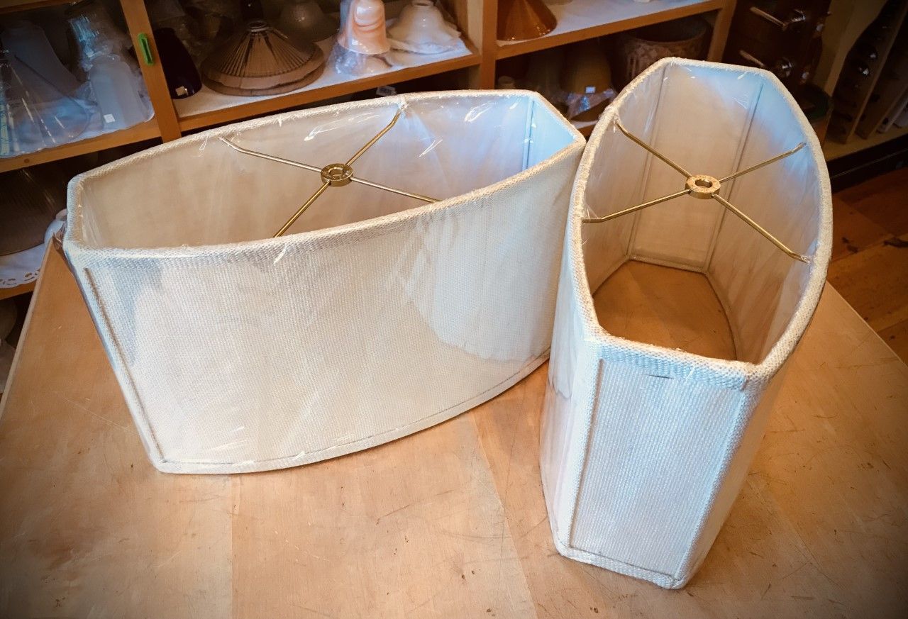 Two off-white fabric lampshades on a wooden surface, one larger than the other.