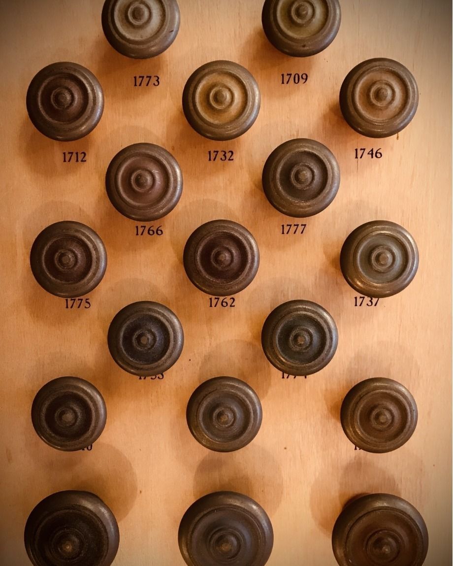 A collection of antique wooden knobs arranged on a light-colored wooden panel with engraved dates.
