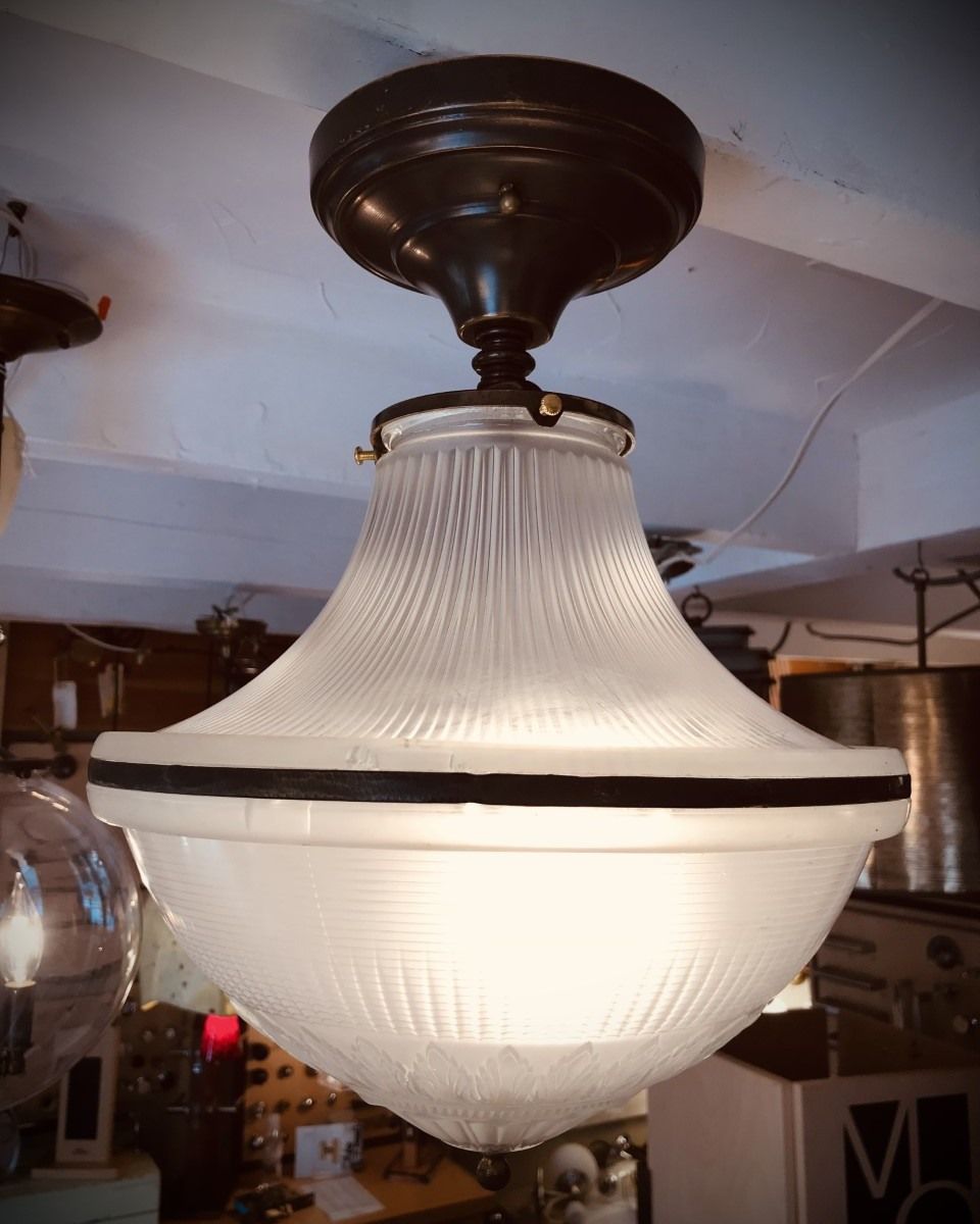 Vintage, frosted glass ceiling light fixture with a black top and band, hanging in a room.