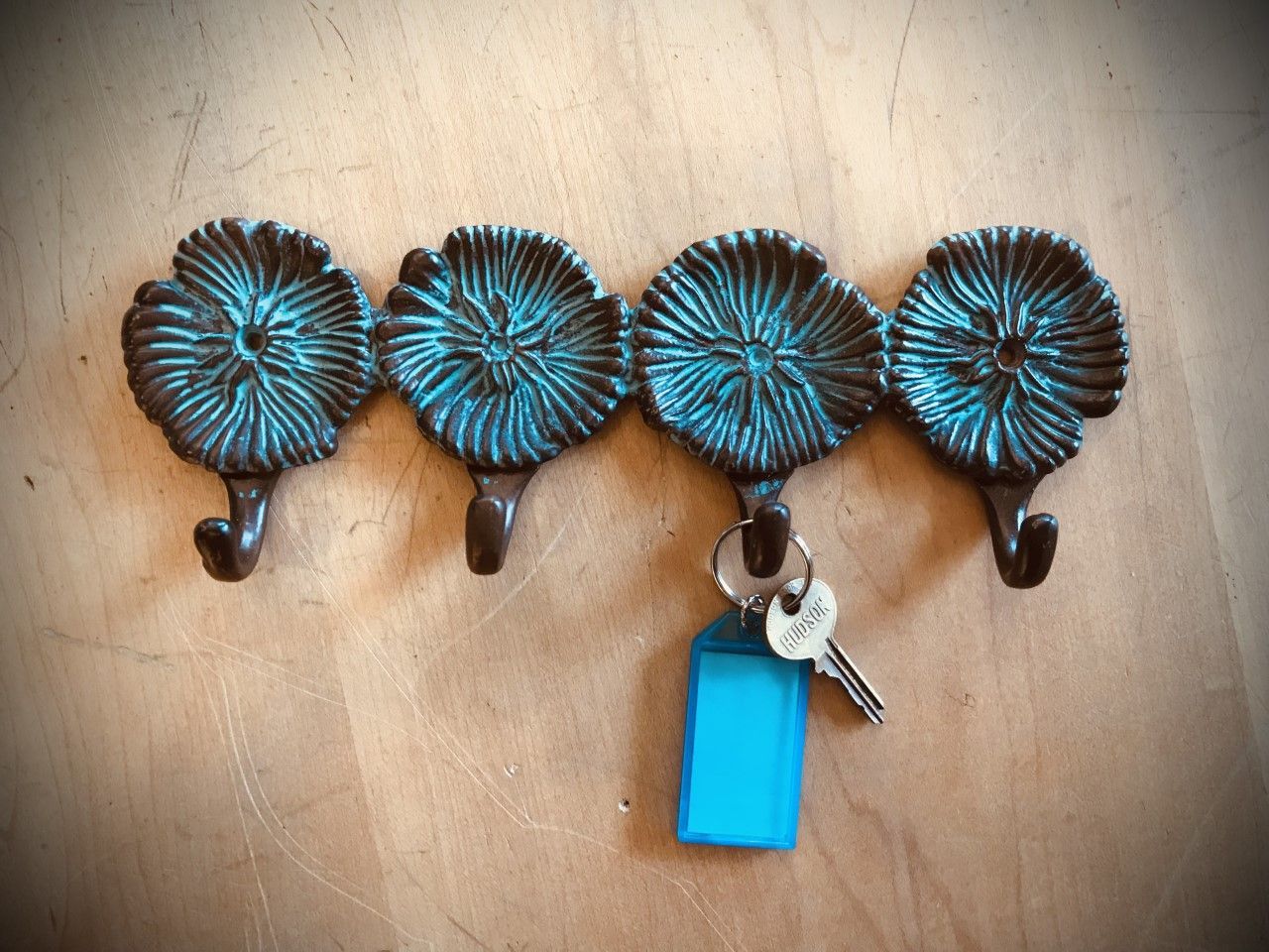 Four-hook key holder with turquoise flower design; one key with a blue tag hanging.