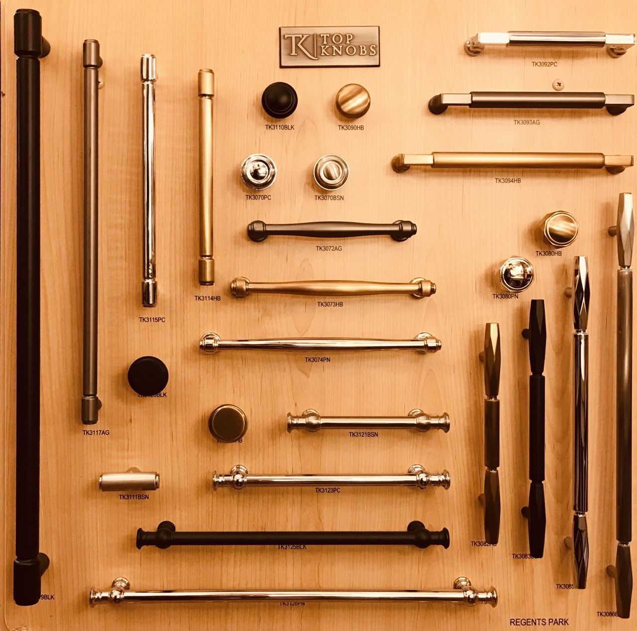 Cabinet hardware display on a wooden board, featuring various knobs and pulls in silver, gold, and black finishes.