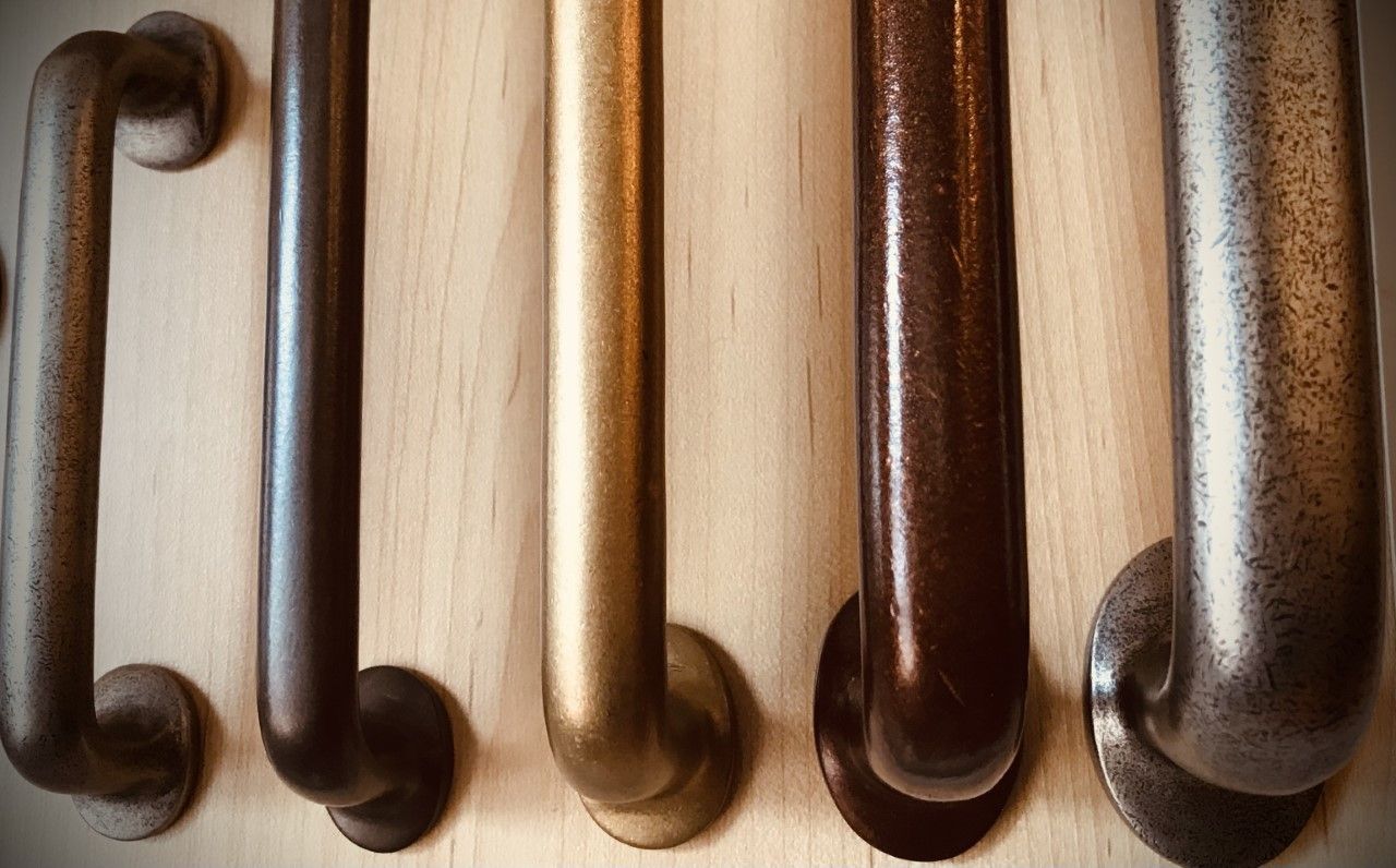 Five metal handles in varying shades of bronze and gold, mounted on a light wood surface.