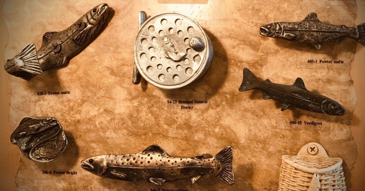 Close-up of fishing-themed decor: a reel, four metal fish, and a creel on a textured backdrop.