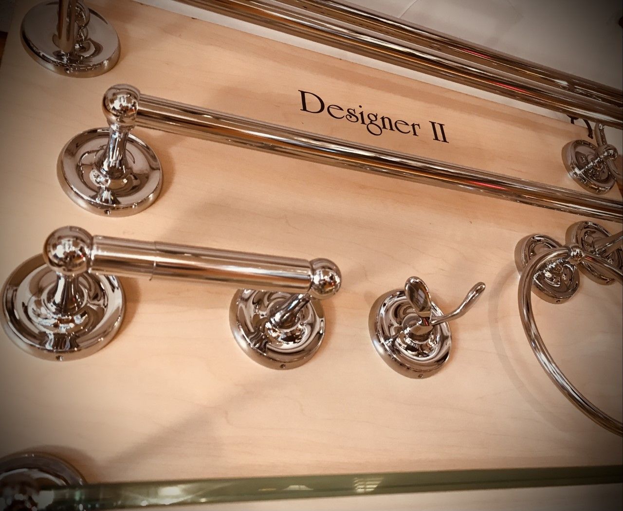 Chrome bathroom accessories displayed on a wooden board. Includes towel bars, toilet paper holder, and a hook.