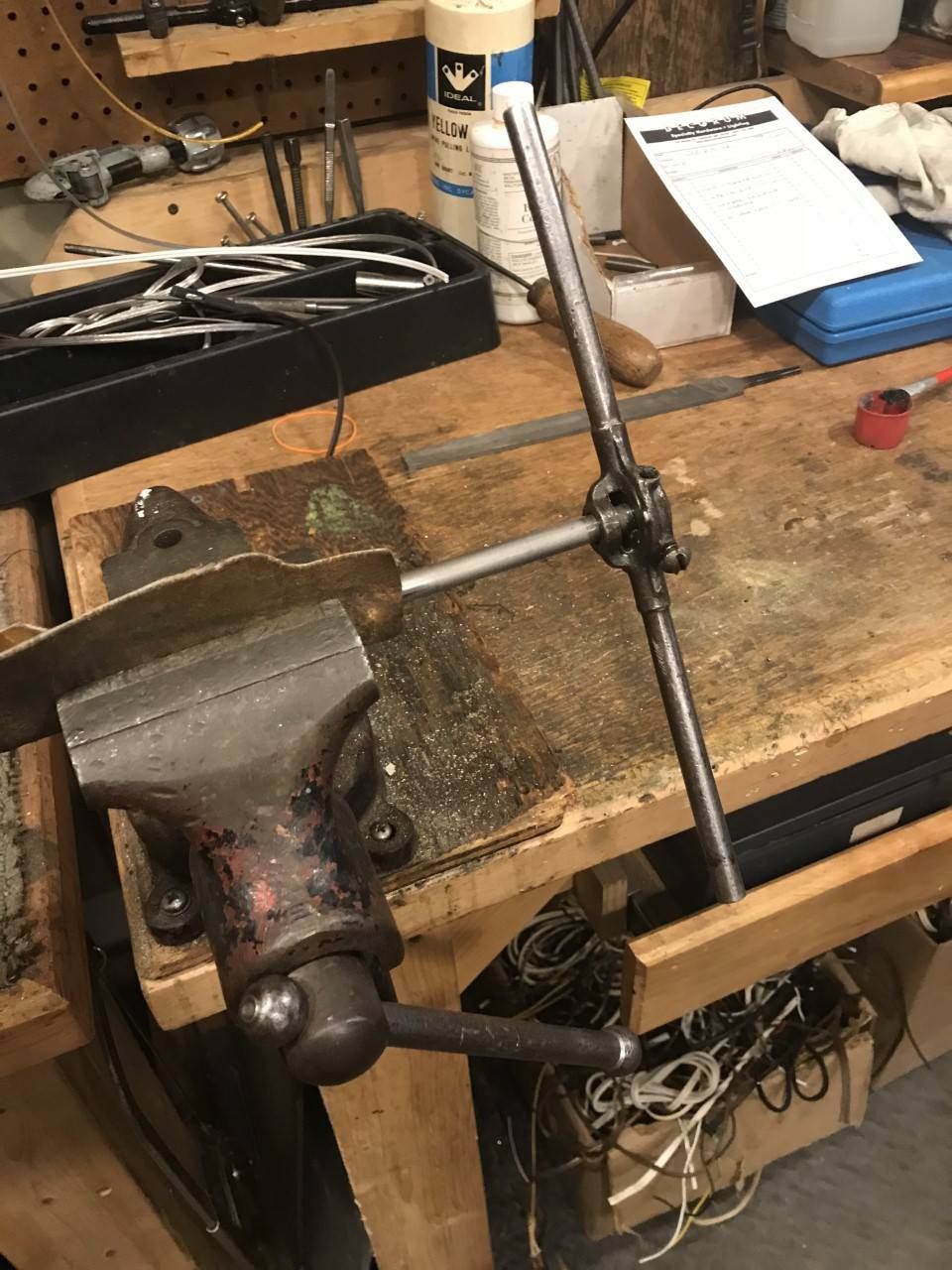 A metal rod held in a vise, with a tap and die set for threading. A workbench is in the background.