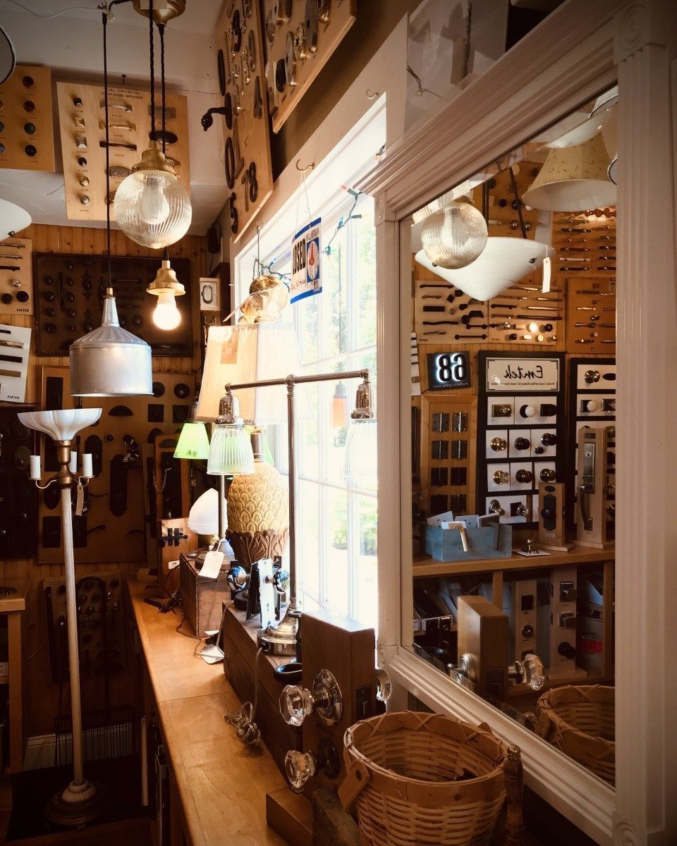 Antique shop interior: diverse lamps and fixtures, wooden shelves, a large mirror, and a window.