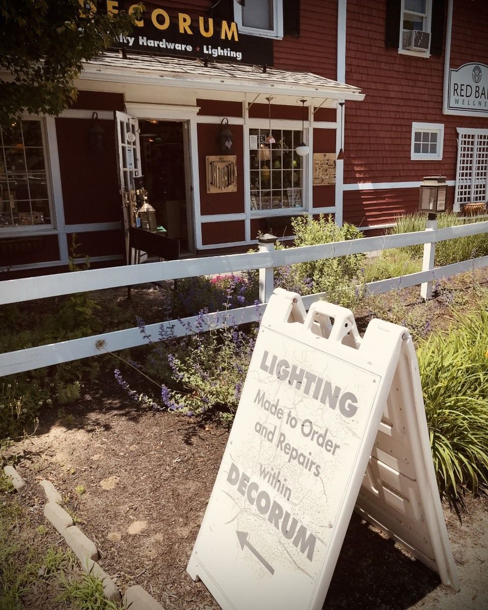 A-frame sign for Decorum Lighting, in front of a red building with a white fence.