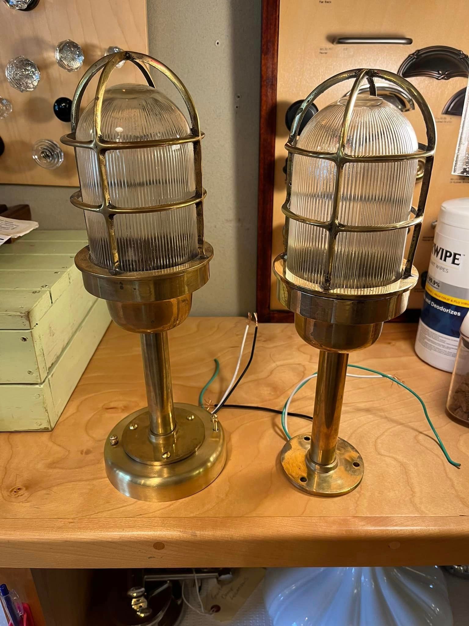 Two brass nautical-style lights with glass globes, sitting on a wooden surface. Wires extend from each.