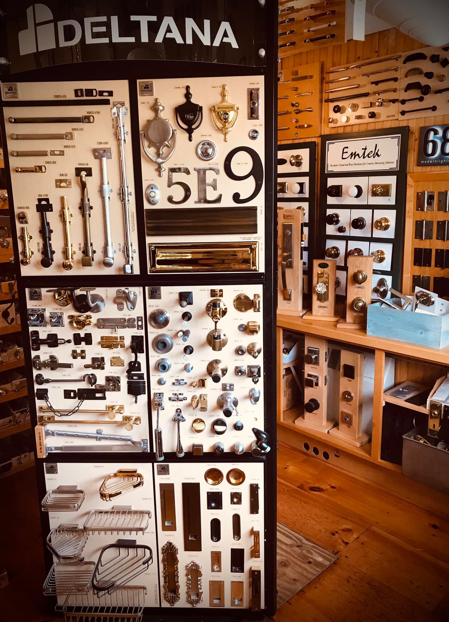 Display of Deltana door hardware, with various knobs, pulls, and plates on wooden boards.