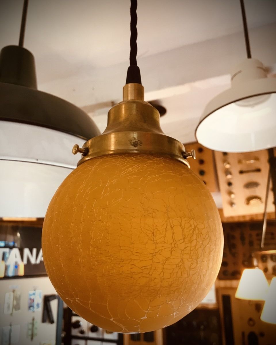 Yellow globe pendant light with brass fixtures, hanging amidst other lamps.