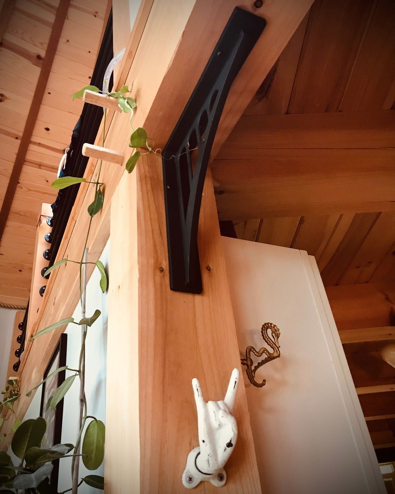 Wooden beams with a decorative black bracket, a white hand-shaped hook, and a brass hook.
