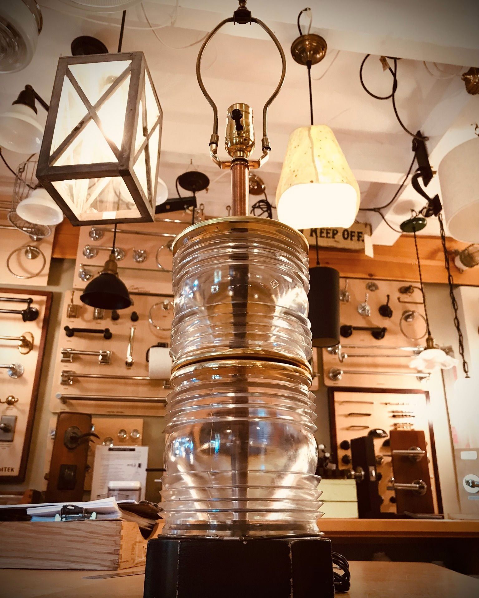 Clear glass lamp with brass accents, in a store with other lighting fixtures and hardware.