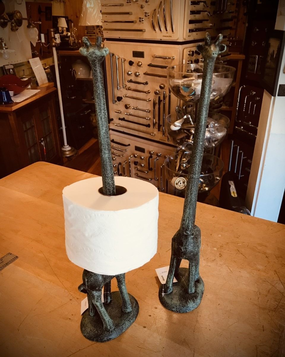 Two giraffe-shaped metal toilet paper holders on a wooden table. One holds a roll of paper.