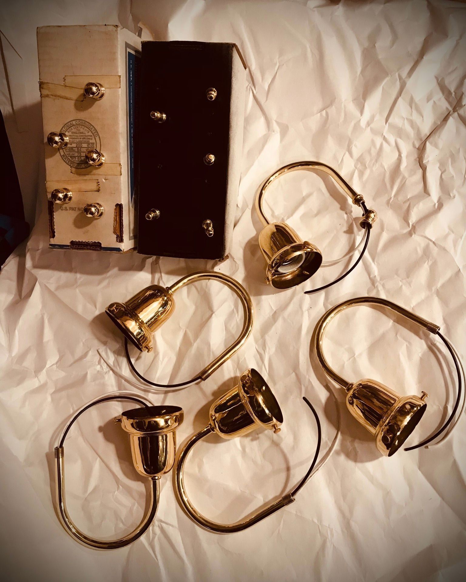 Gold-toned bell-shaped light fixtures with electrical wiring, next to two boxes on crumpled white paper.