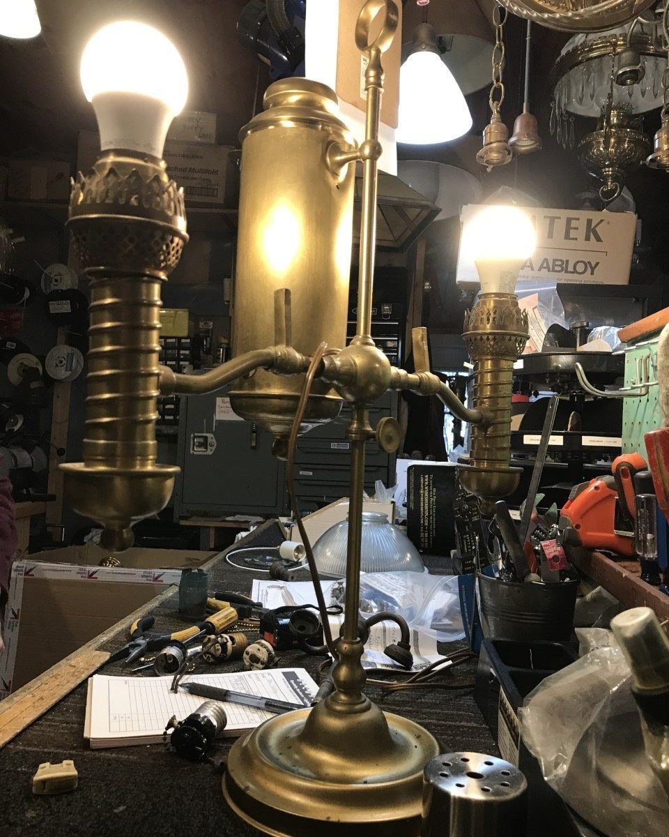 Brass desk lamp with three light fixtures, on a cluttered workbench.