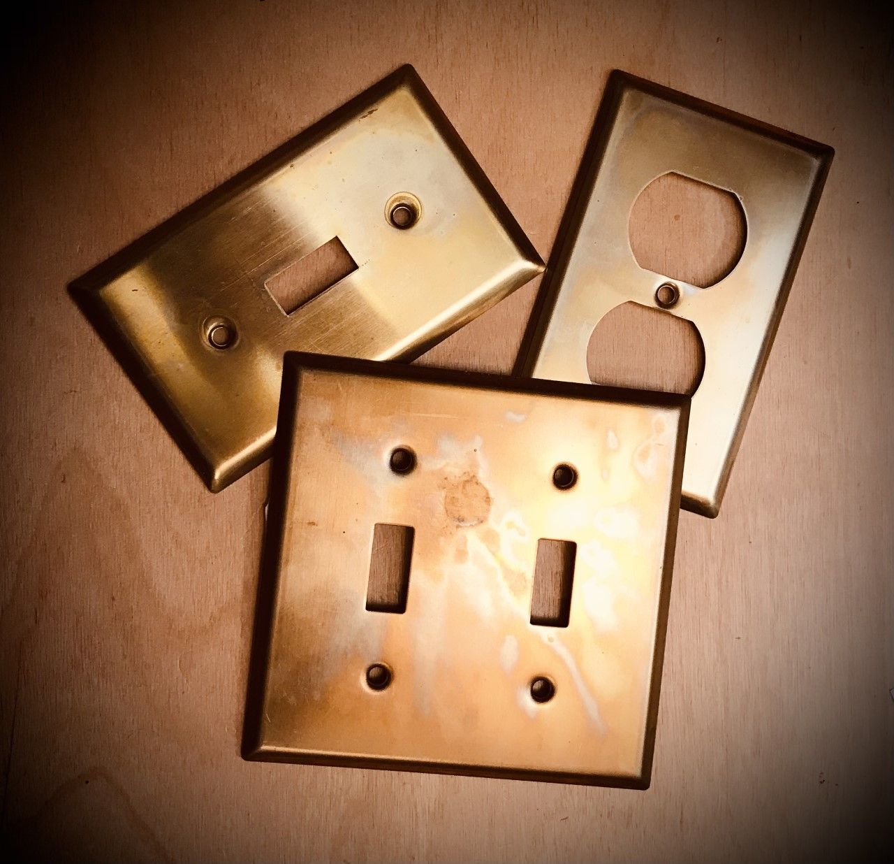 Three brass electrical switch plates on a light wooden surface.