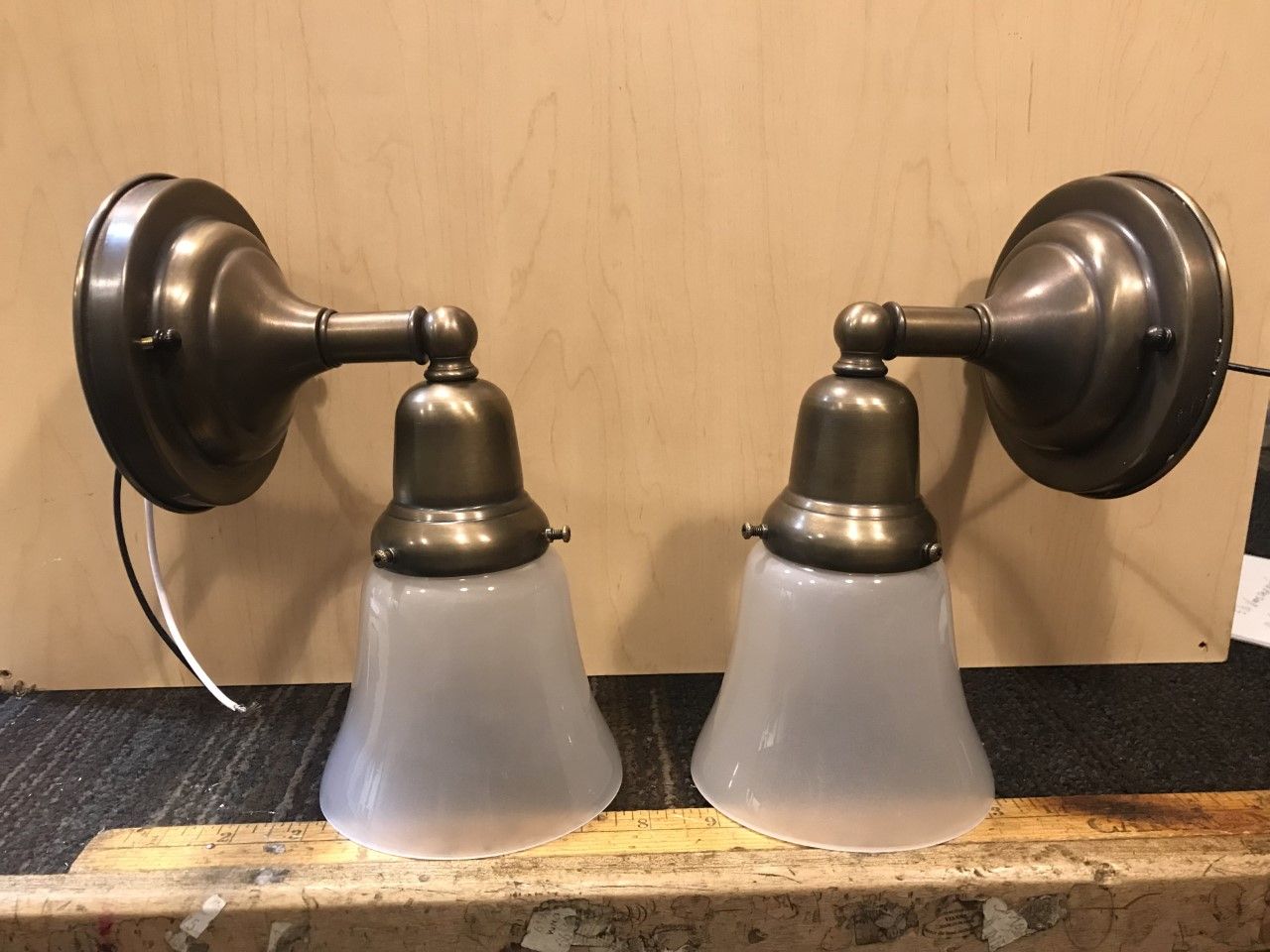 Two antique bronze-toned wall sconces with frosted glass shades, on a wooden surface.