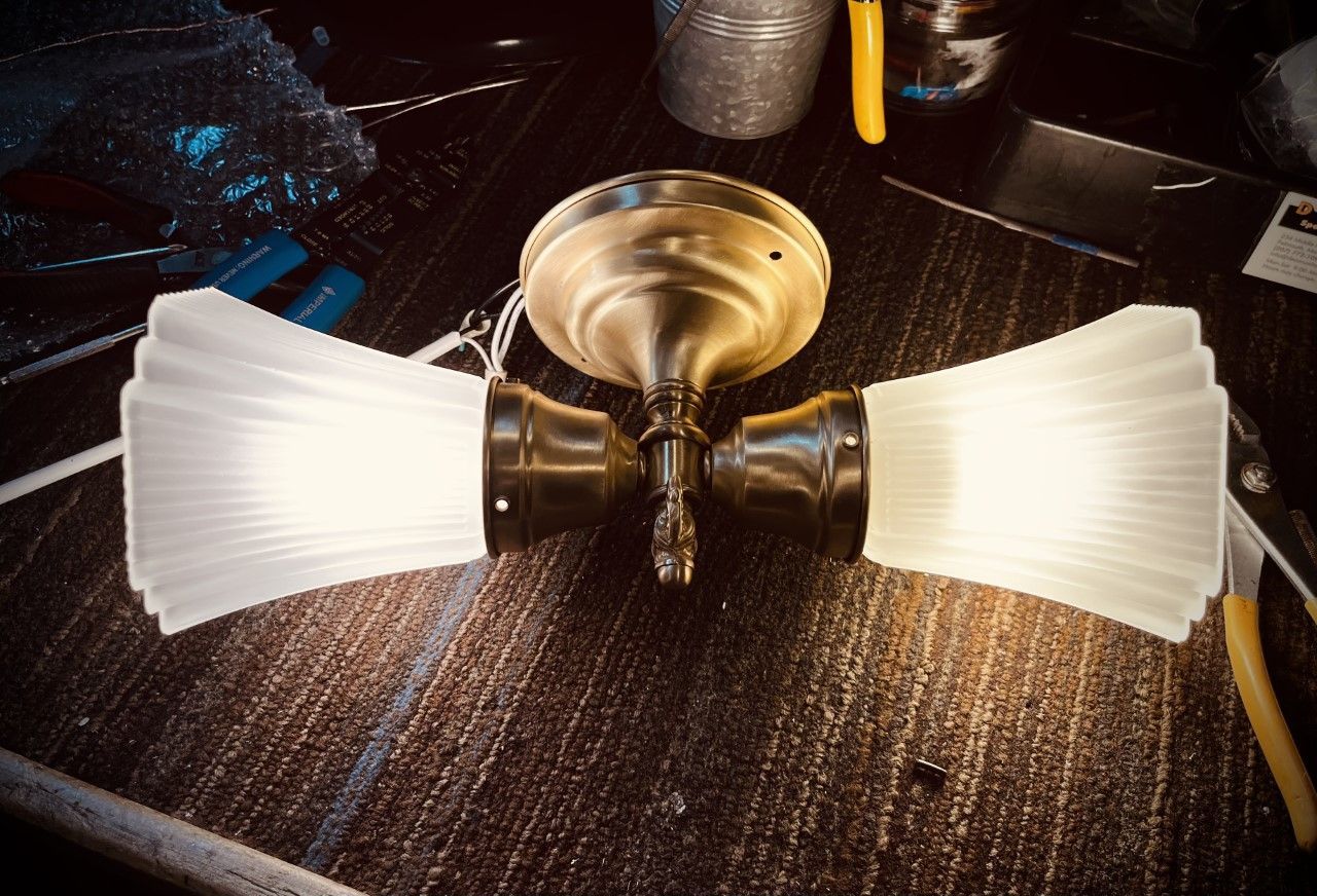 Brass ceiling light fixture with two frosted glass shades, resting on a dark wood surface.