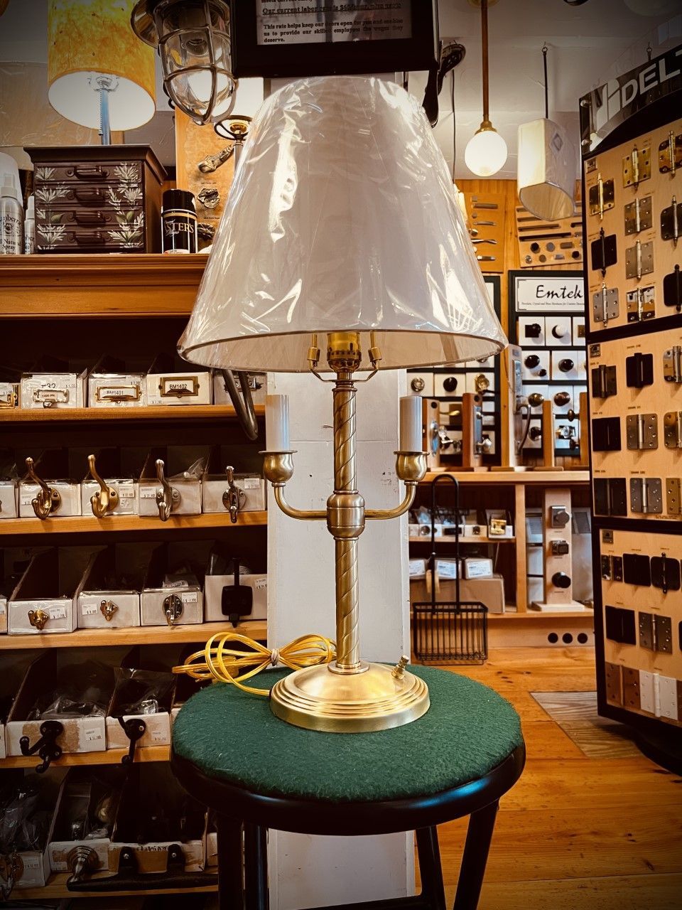 Brass table lamp with a white shade, on a green stool, inside a store.