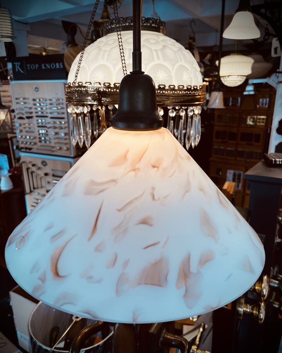 White and peach-swirled glass pendant light with a dark metal fixture, hanging in a store.