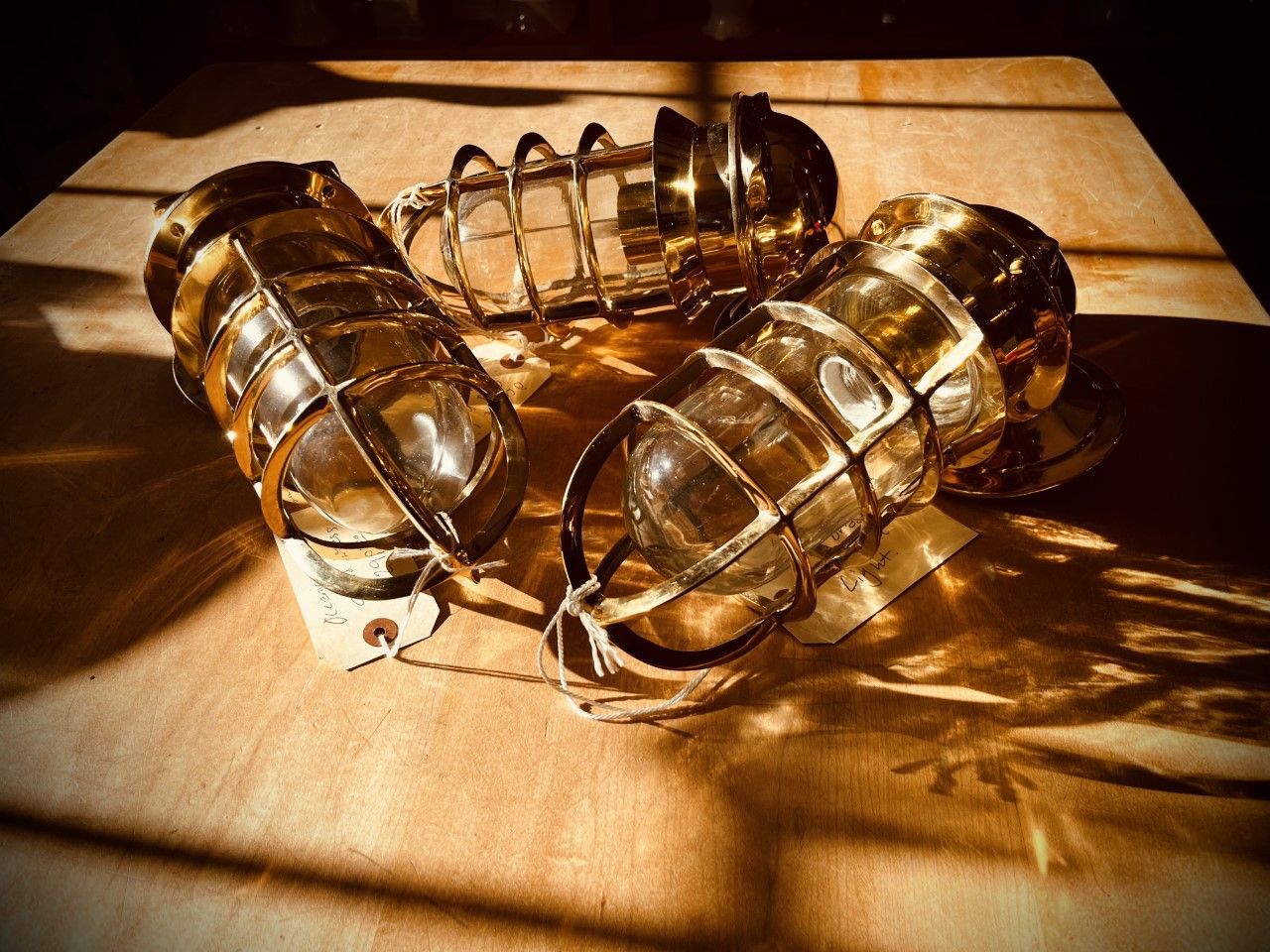 Three brass caged nautical lights on a wooden surface, casting shadows.
