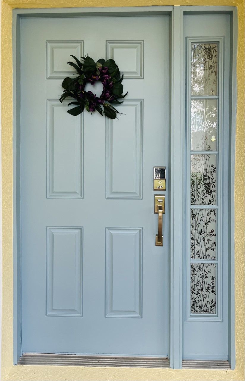 Light blue front door with wreath and side window with decorative glass.