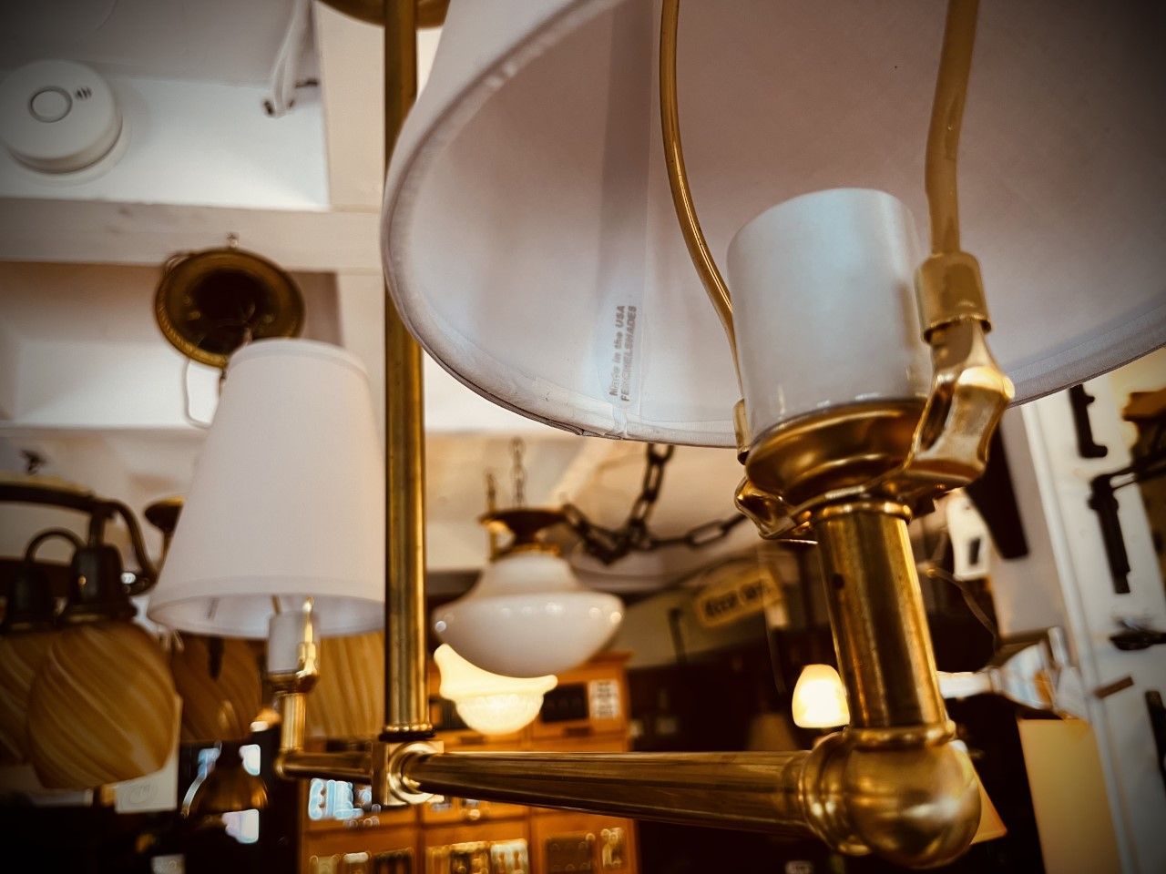 Close-up of a gold-toned lamp fixture with two white lampshades and a visible light bulb socket; a shop interior.