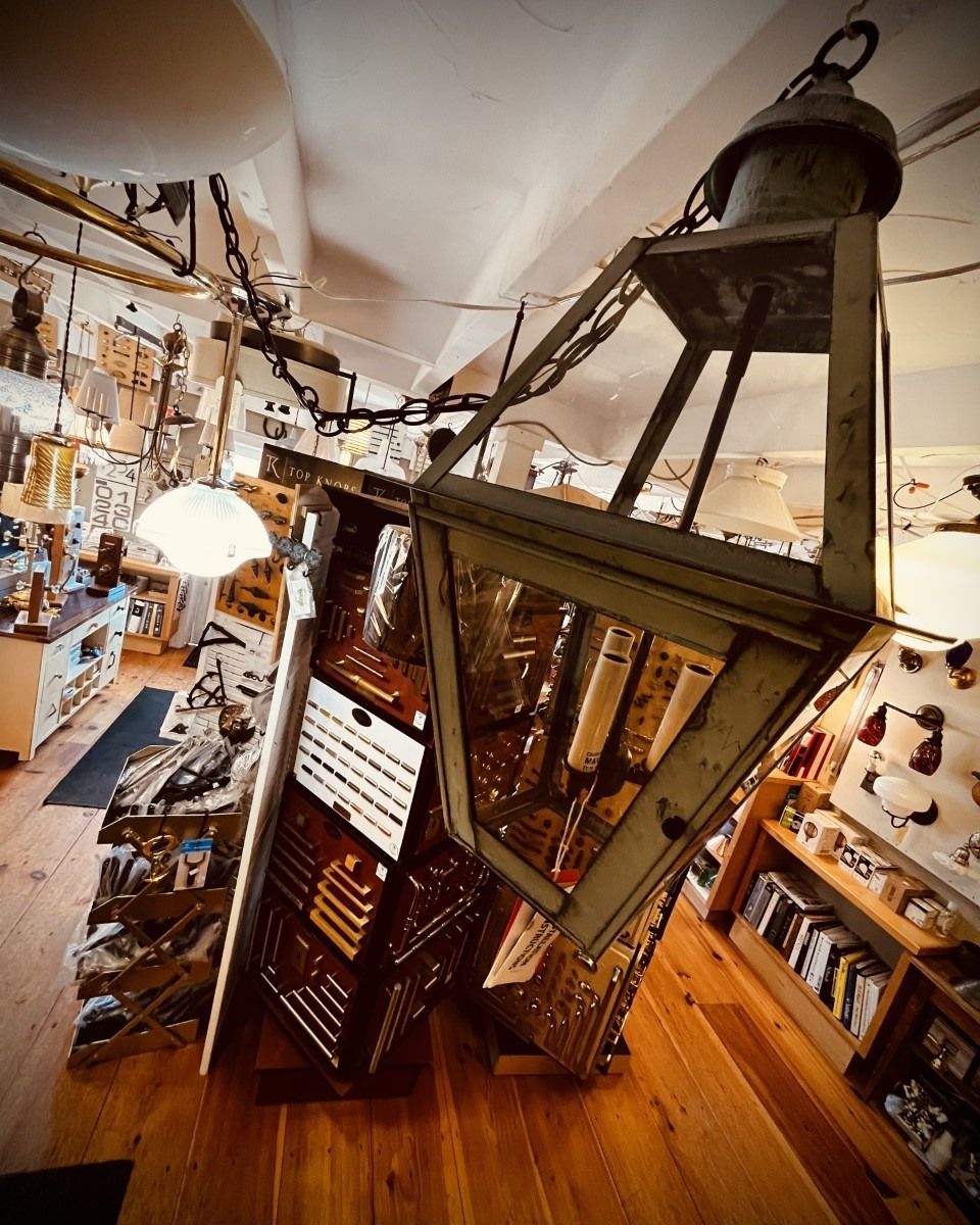 Large antique lantern hanging in a shop with wooden floors and cluttered shelves.