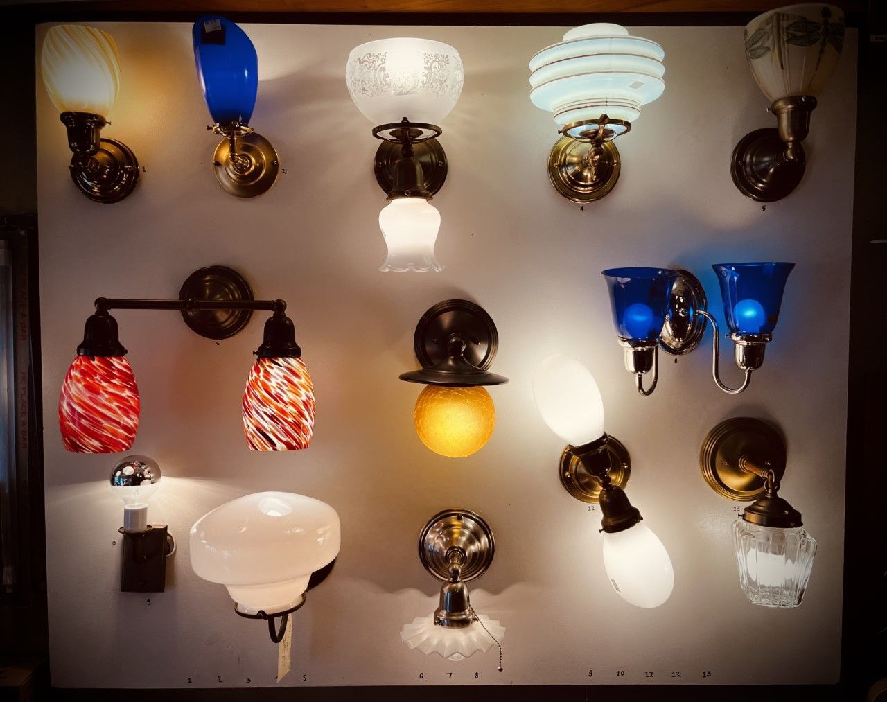 Variety of antique wall sconces, showcasing different shapes and colored glass shades, mounted on a wall.