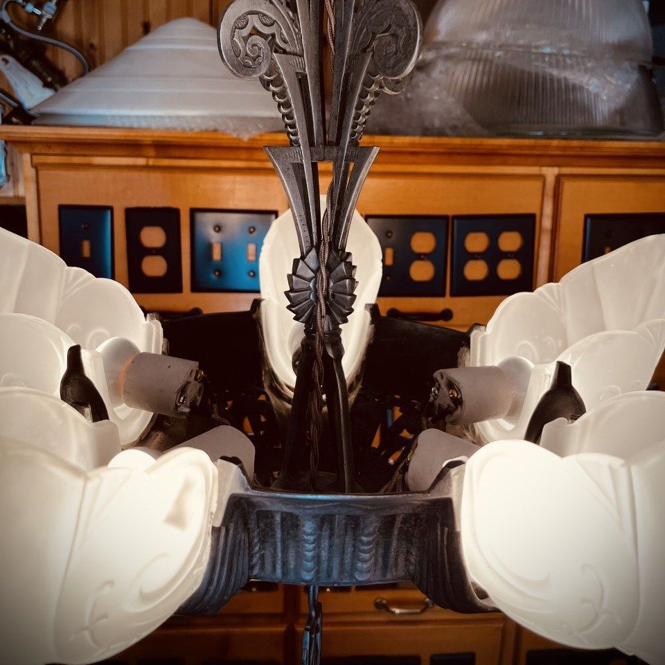 Ornate Art Deco chandelier with white glass shades and dark metal frame.