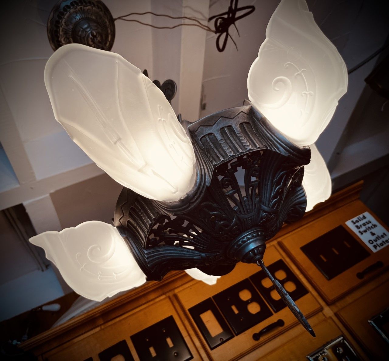 Antique ceiling fan with art deco style frosted glass blades; above wooden cabinet.