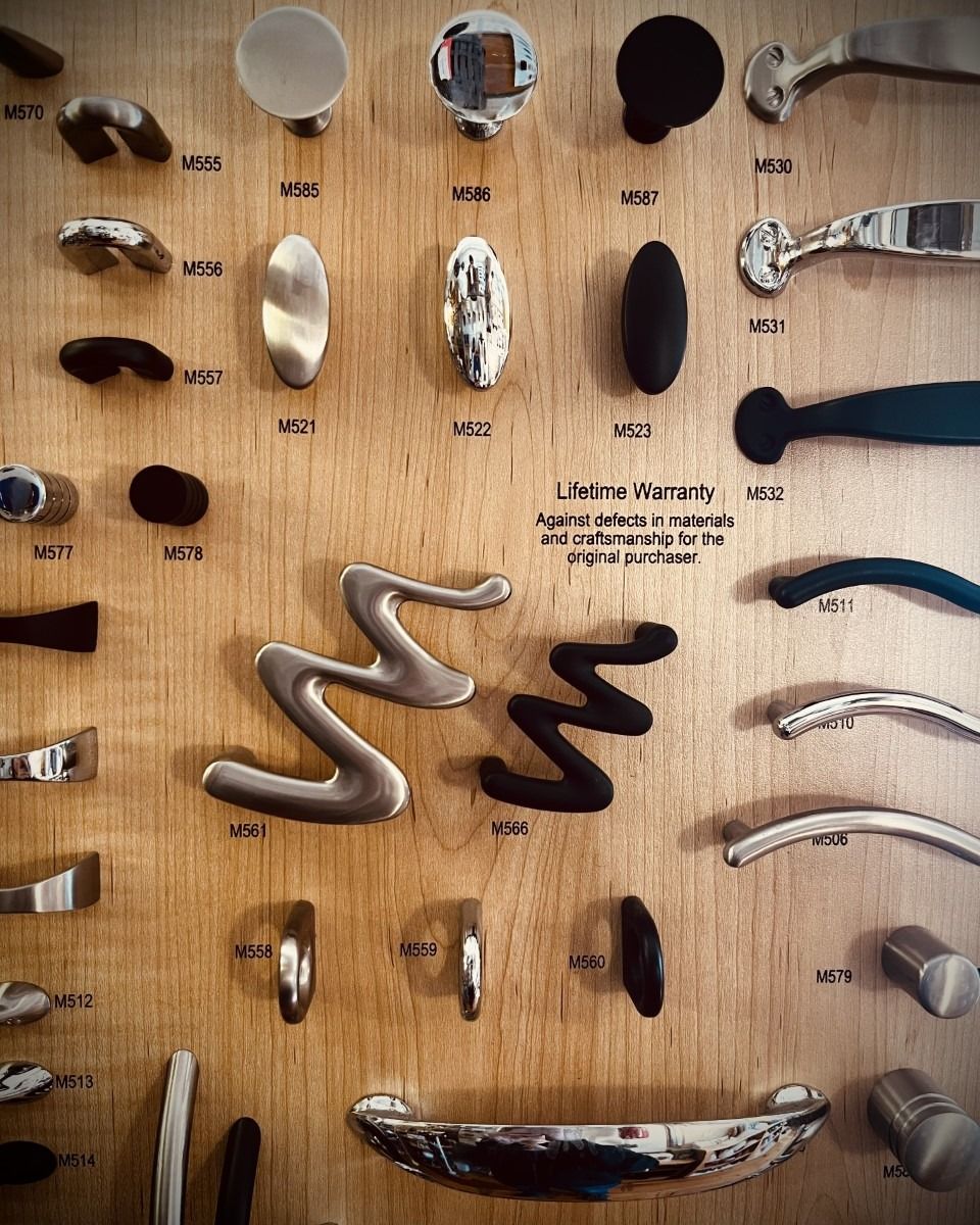 Cabinet hardware display on a wooden board, featuring various knobs and pulls in silver and black finishes.