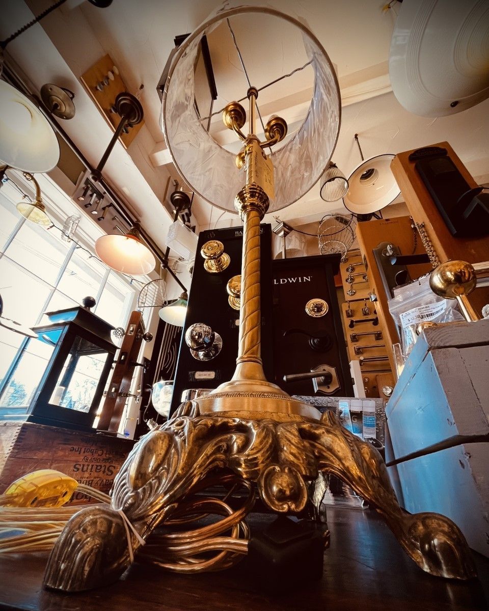 Ornate brass lamp with claw feet in a shop filled with vintage lighting fixtures.