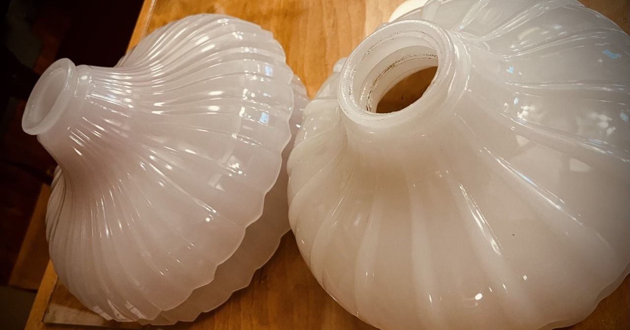 Two white, ribbed, glass light shades on a wooden surface.