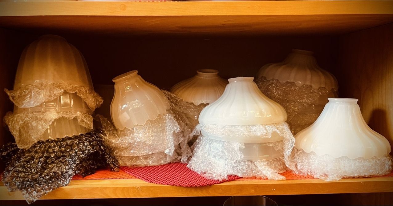 Shelf with various clear and white glass lampshades, some with decorative edges.