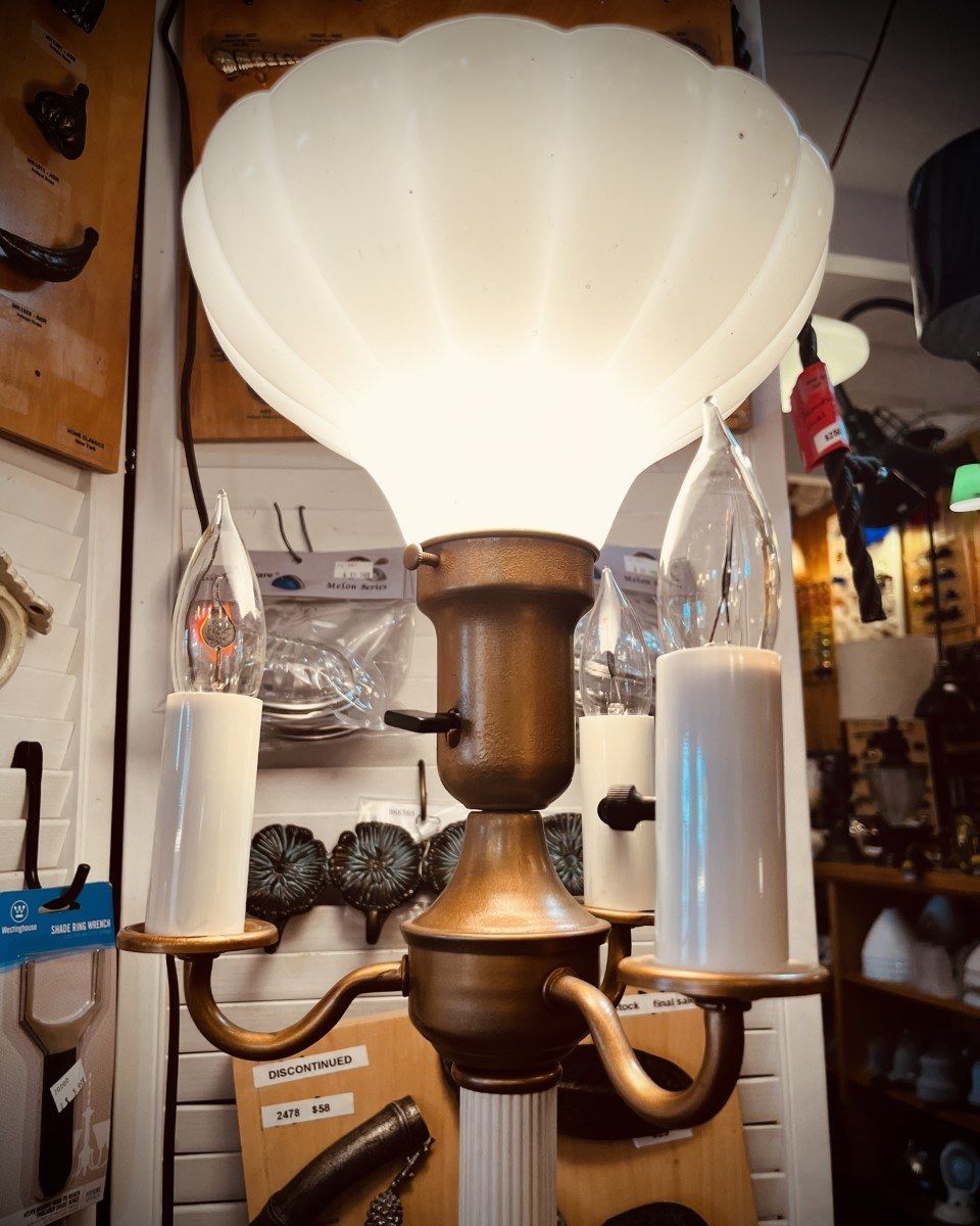 Antique brass lamp with a white scalloped shade and two candle-shaped bulbs.