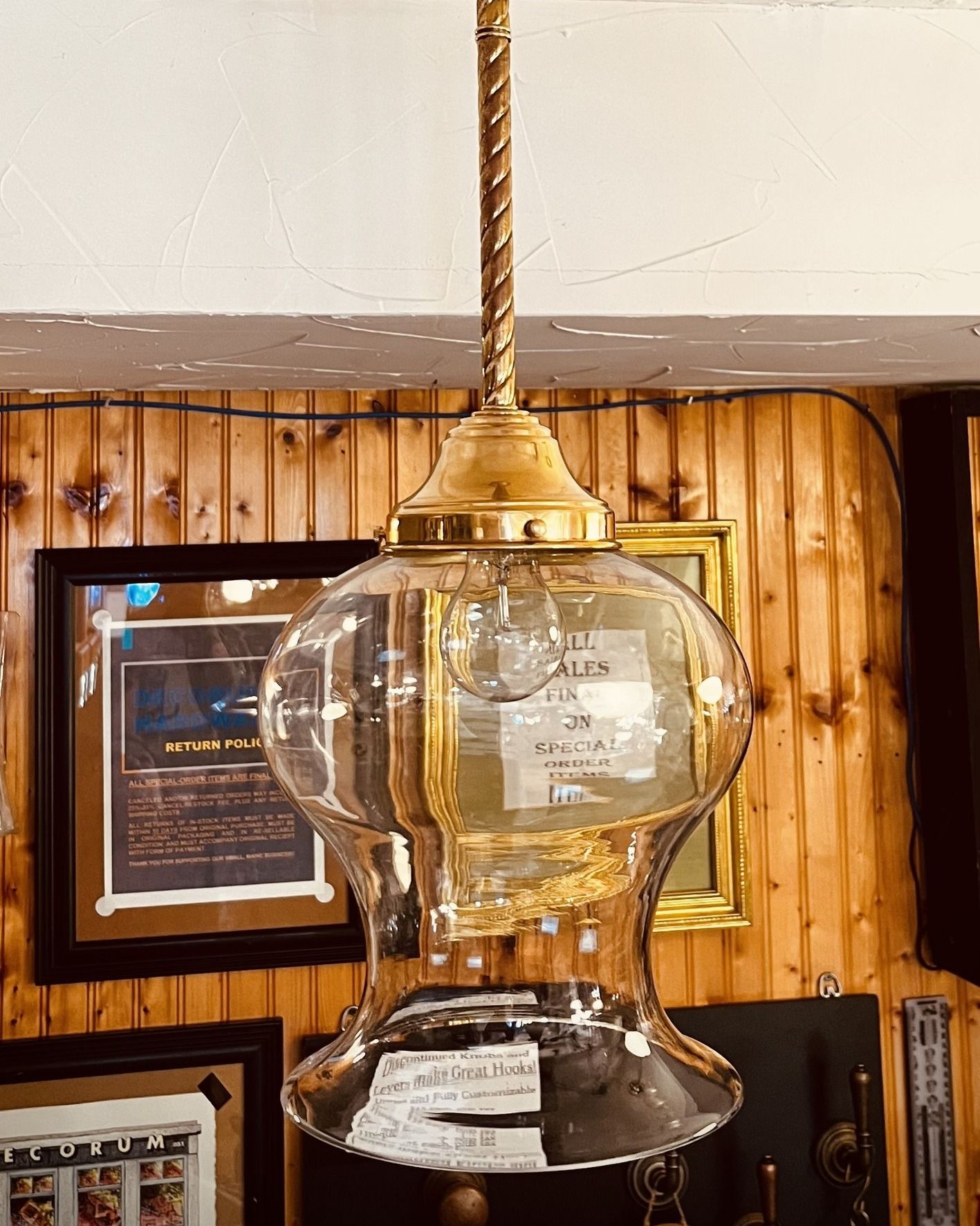 Antique glass pendant lamp with brass accents hanging indoors near wooden paneling.